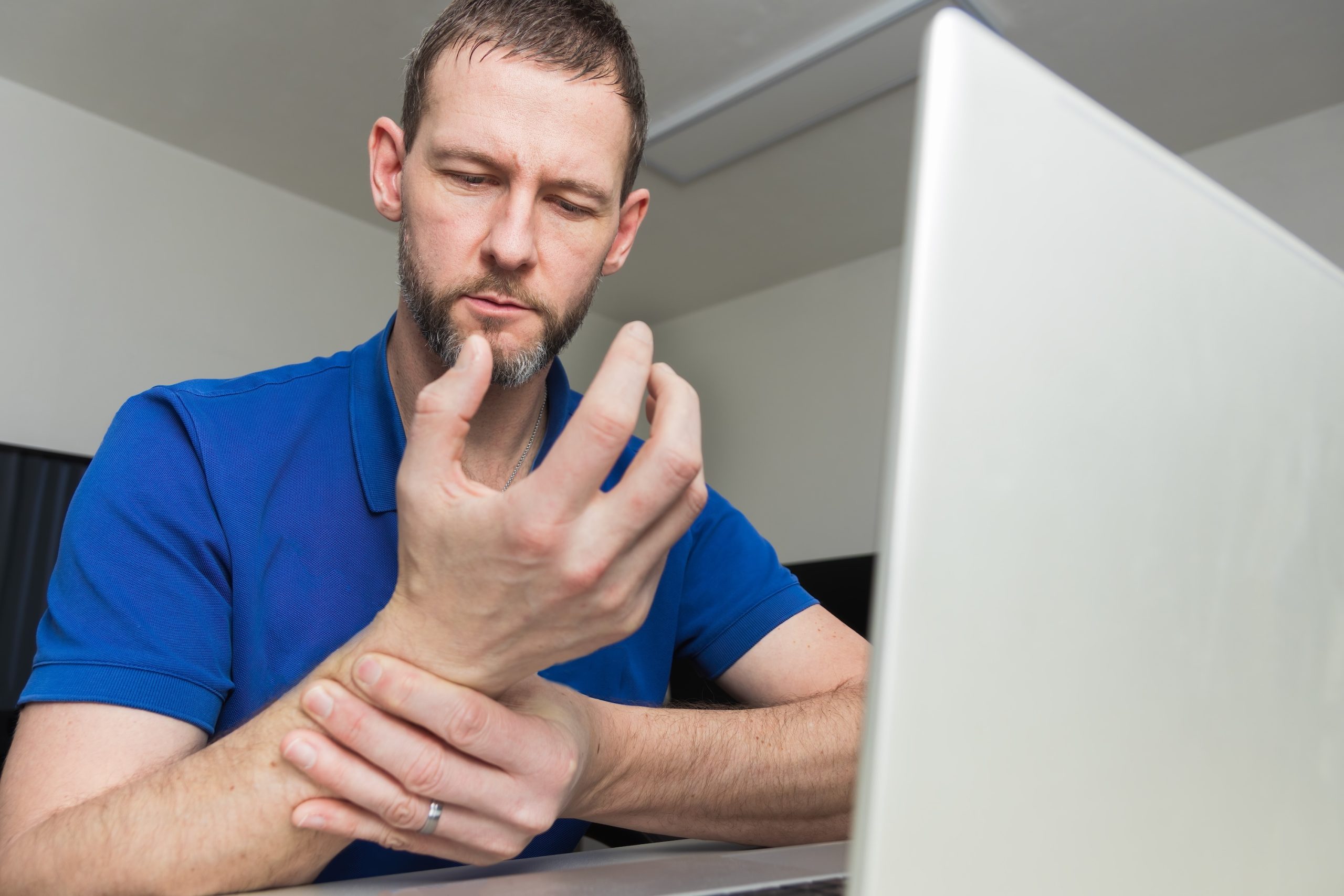Junger Mann hält sich das Handgelenk fest, während er am Computer arbeitet. Beispielfoto für Karpaltunnel-Erkrankung, Neurologische Praxis Dr. Hartmut Bauer, Euskirchen Junger Mann hält sich das Handgelenk fest, während er am Computer arbeitet. Beispielfoto für Karpaltunnel-Erkrankung, Neurologische Praxis Dr. Hartmut Bauer, Euskirchen
